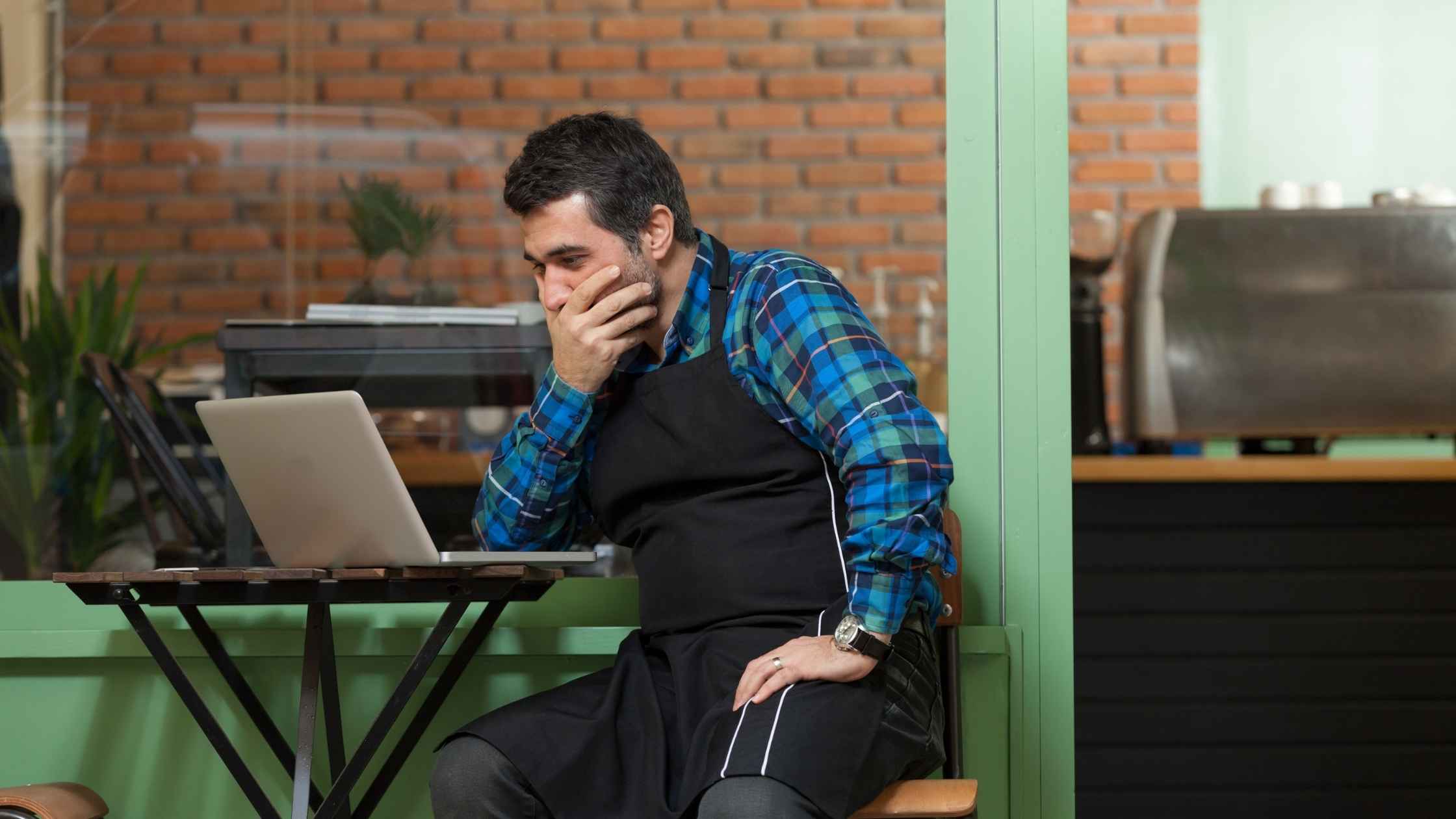 Stressed business owner reviewing laptop, seeking strategic advice.