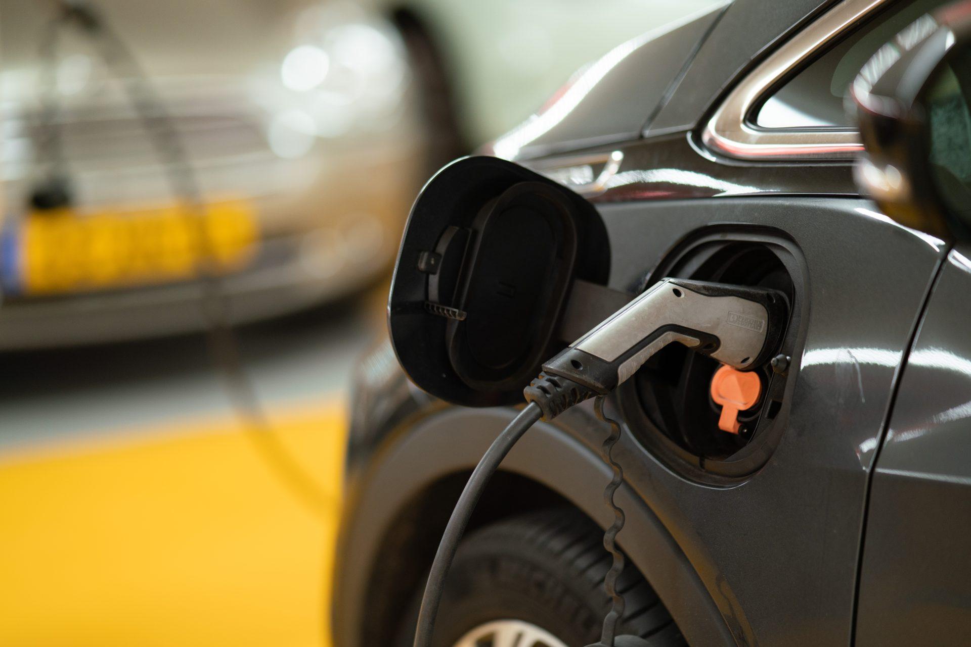 Electric car charging at a station with a plugged-in charger, focusing on the charging port and cable.