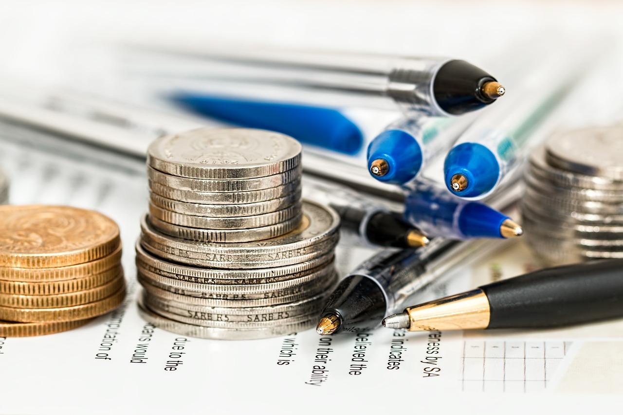 Stacks of coins and several ballpoint pens on top of financial documents.