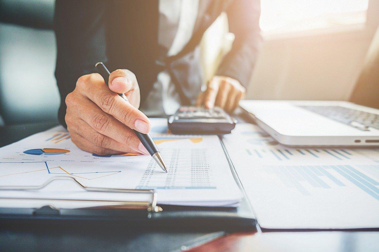 Businessperson analyzing financial charts and graphs, using a calculator and laptop, focusing on data and statistics.