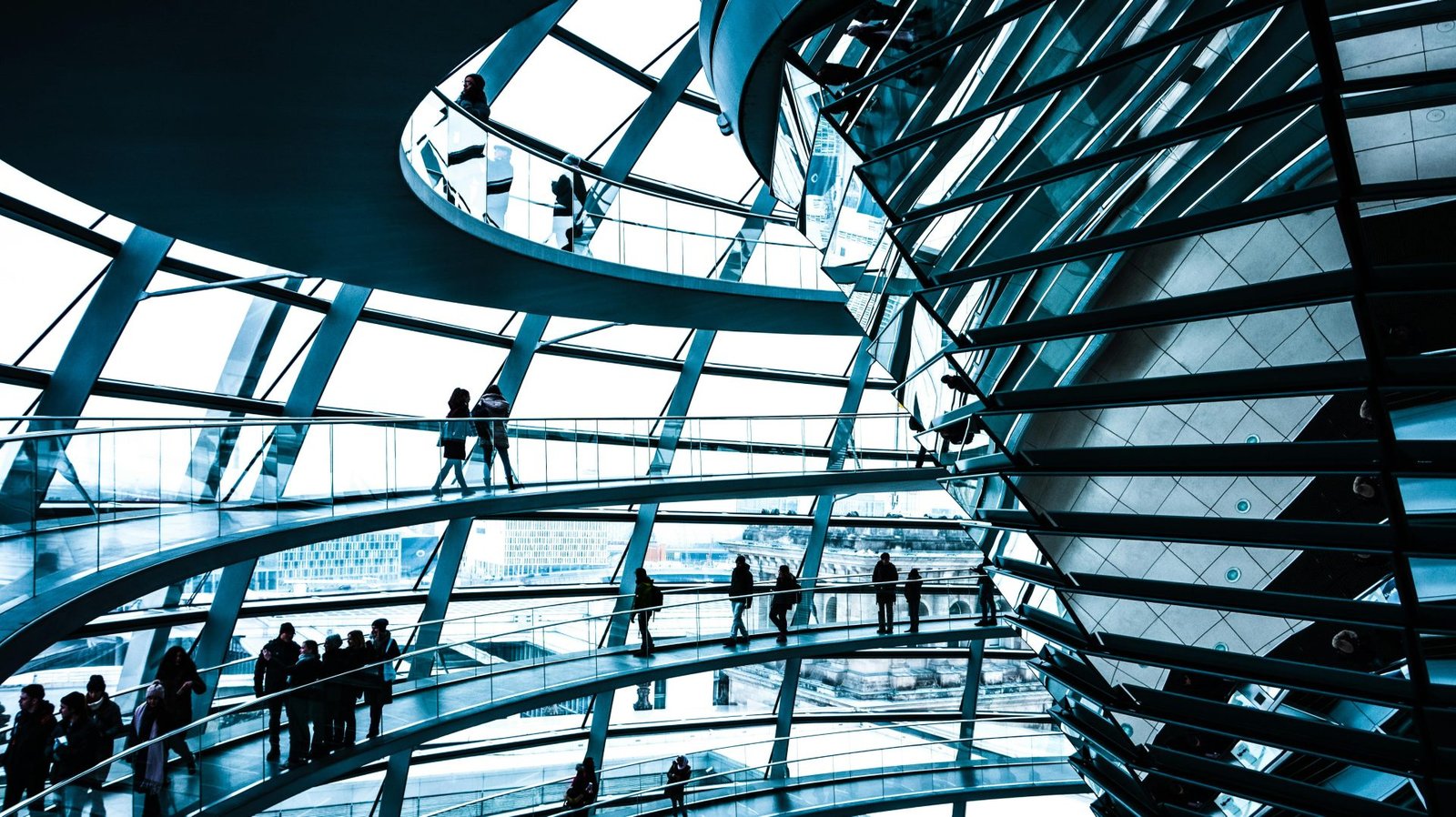 Interior view of a modern building with multiple curved walkways and people walking along them, featuring large glass windows.