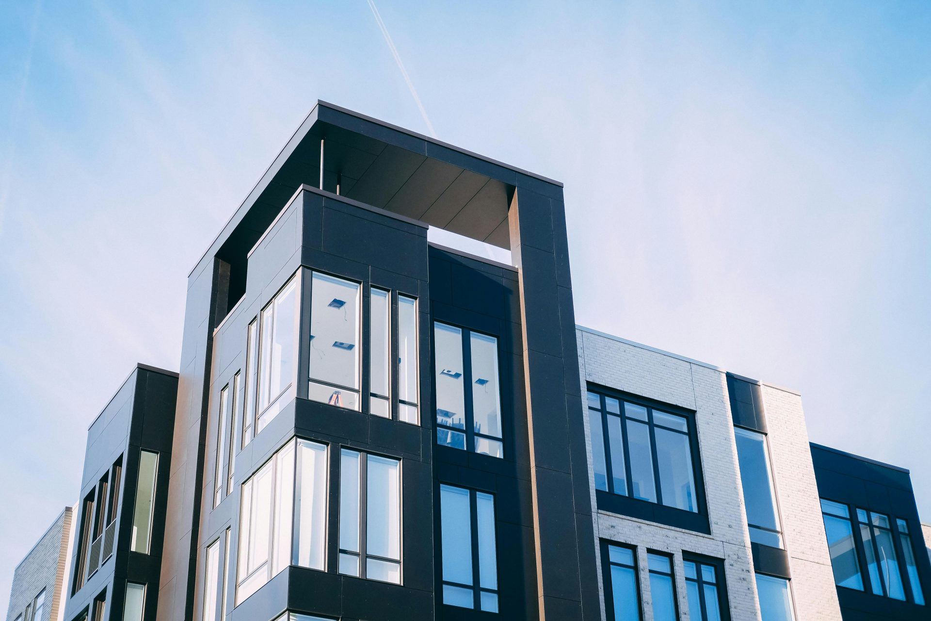 Modern multi-story apartment building with large windows and a mix of black and white facades under a clear blue sky.