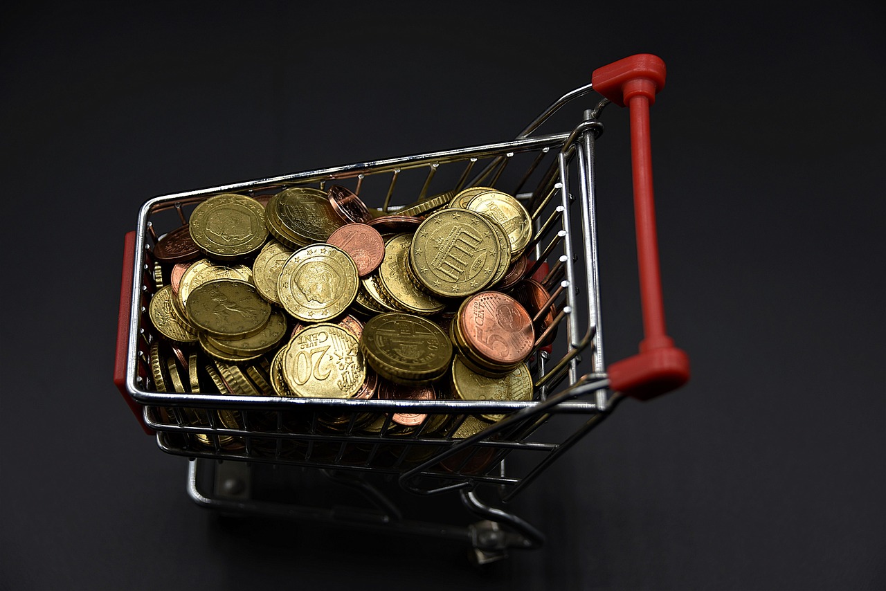 Miniature shopping cart filled with various euro coins on a dark background.