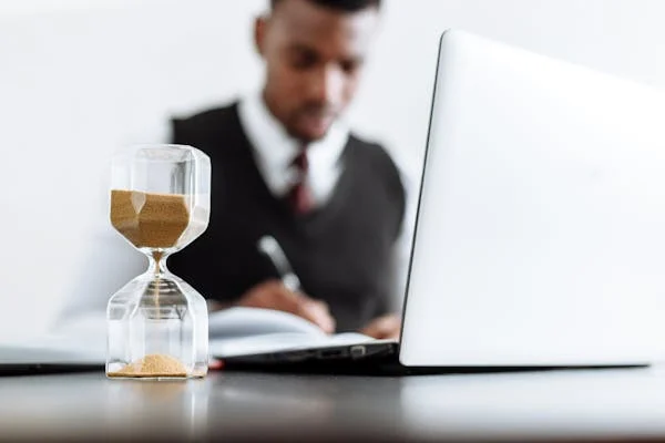 Man working at laptop with hourglass beside him, symbolizing time management for commonwealth superannuation test tax.