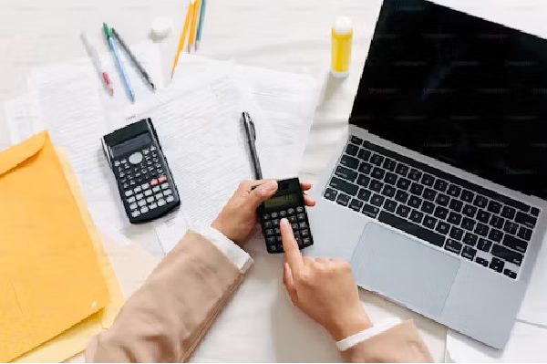 Person calculating domicile test tax with a laptop, papers, and two calculators on a desk.