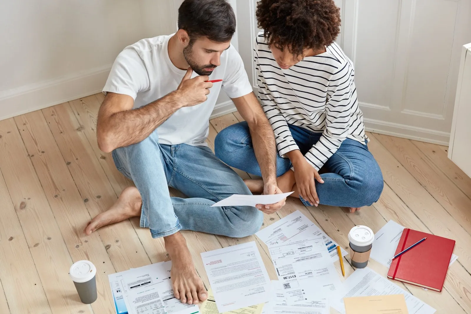 Couple sitting on floor reviewing documents for estate planning checklist with coffee cups nearby.