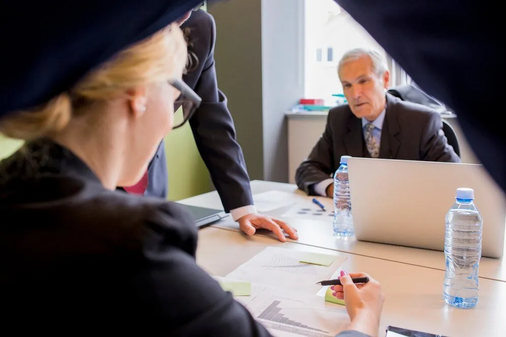 Businesspeople review documents at a meeting, discussing a legal case.