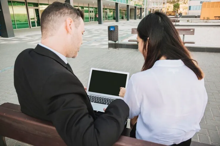 Two businesspeople review a laptop, discussing NSW strata meeting recordings and implied consent under the Surveillance Devices Act.