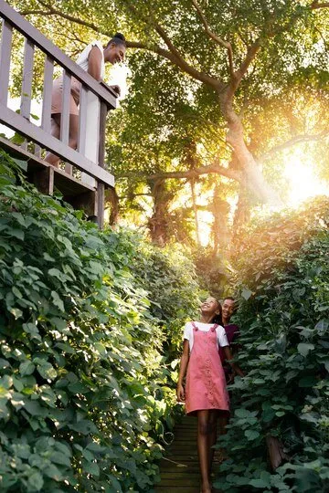 Happy family walking on path through lush green foliage, sunlight streaming through trees.