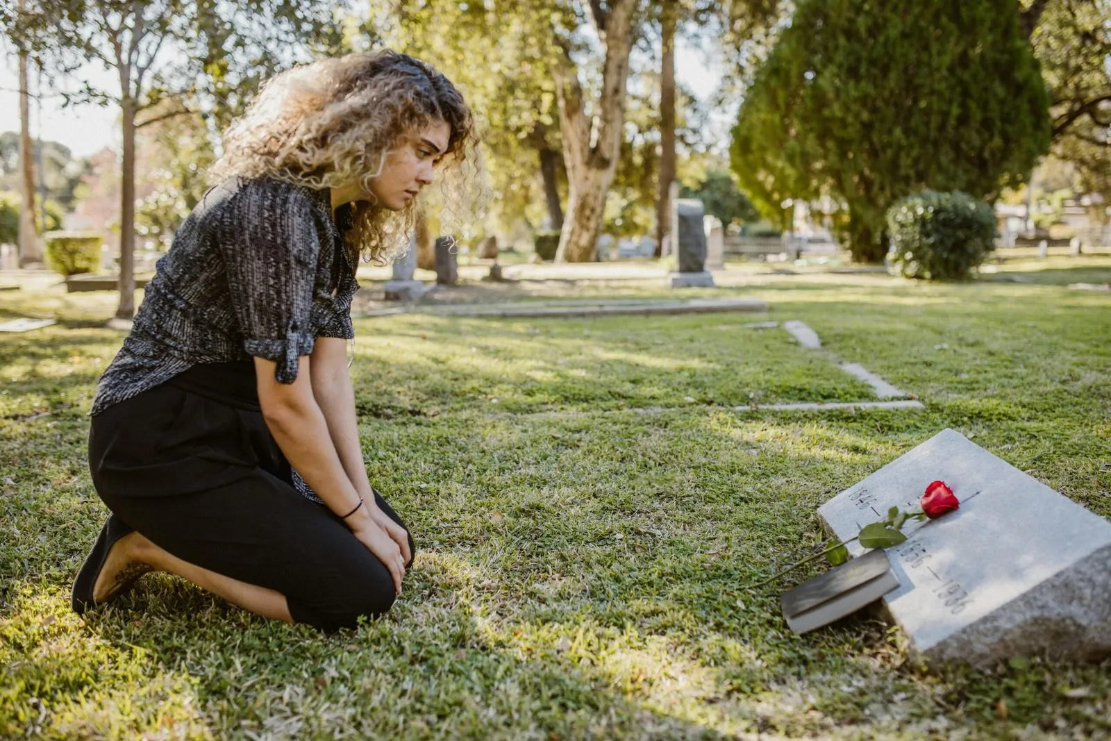 Woman kneeling at a gravesite, placing a rose and book.