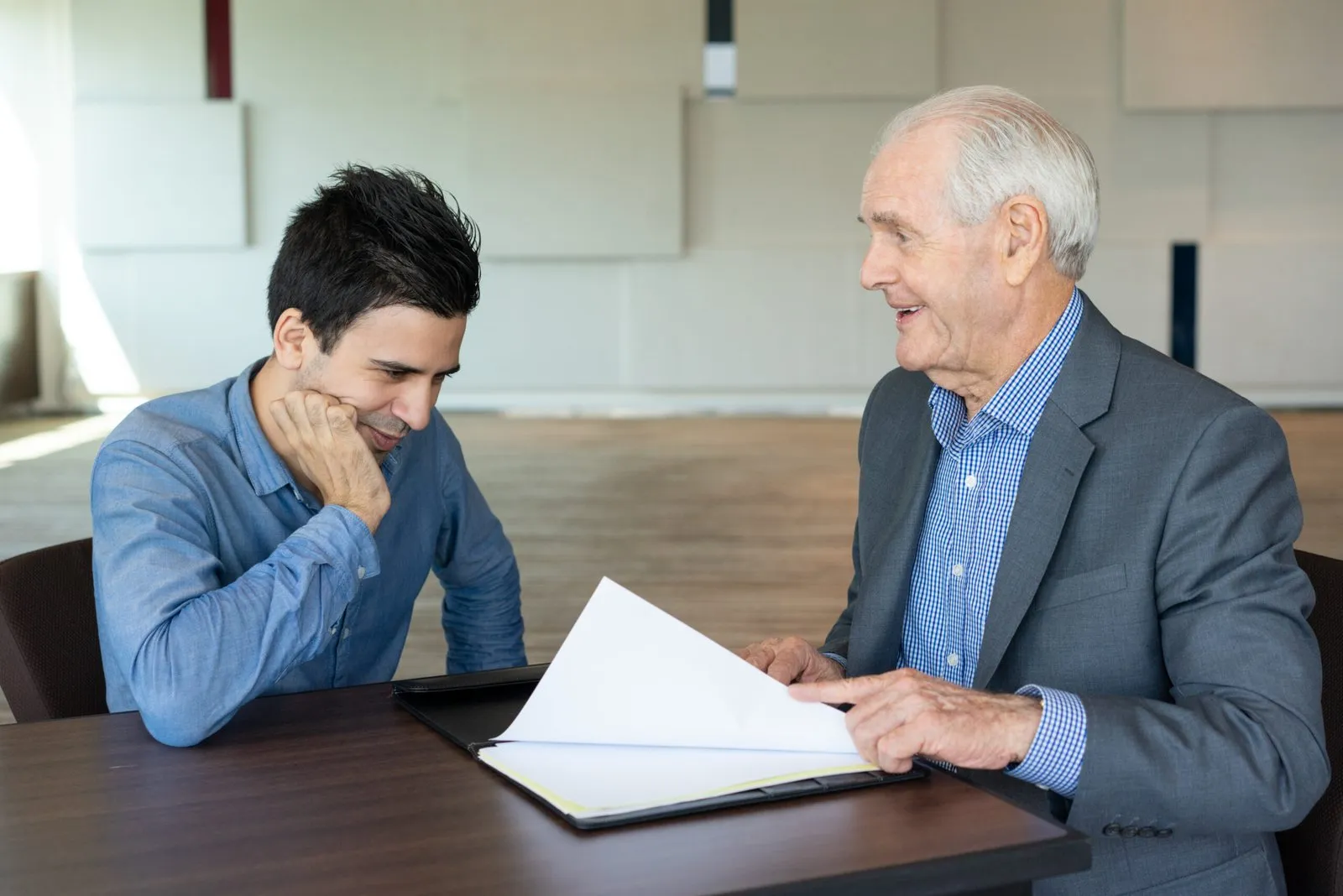 Two men discussing documents at a table in an office