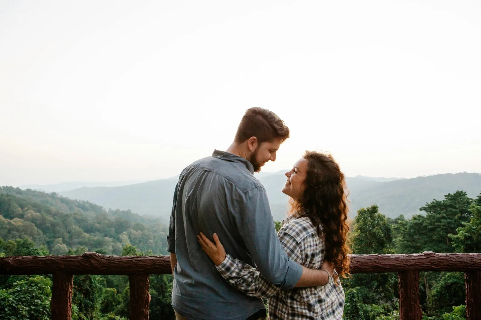 Couple embracing on a balcony overlooking a mountain range, enjoying the view.
