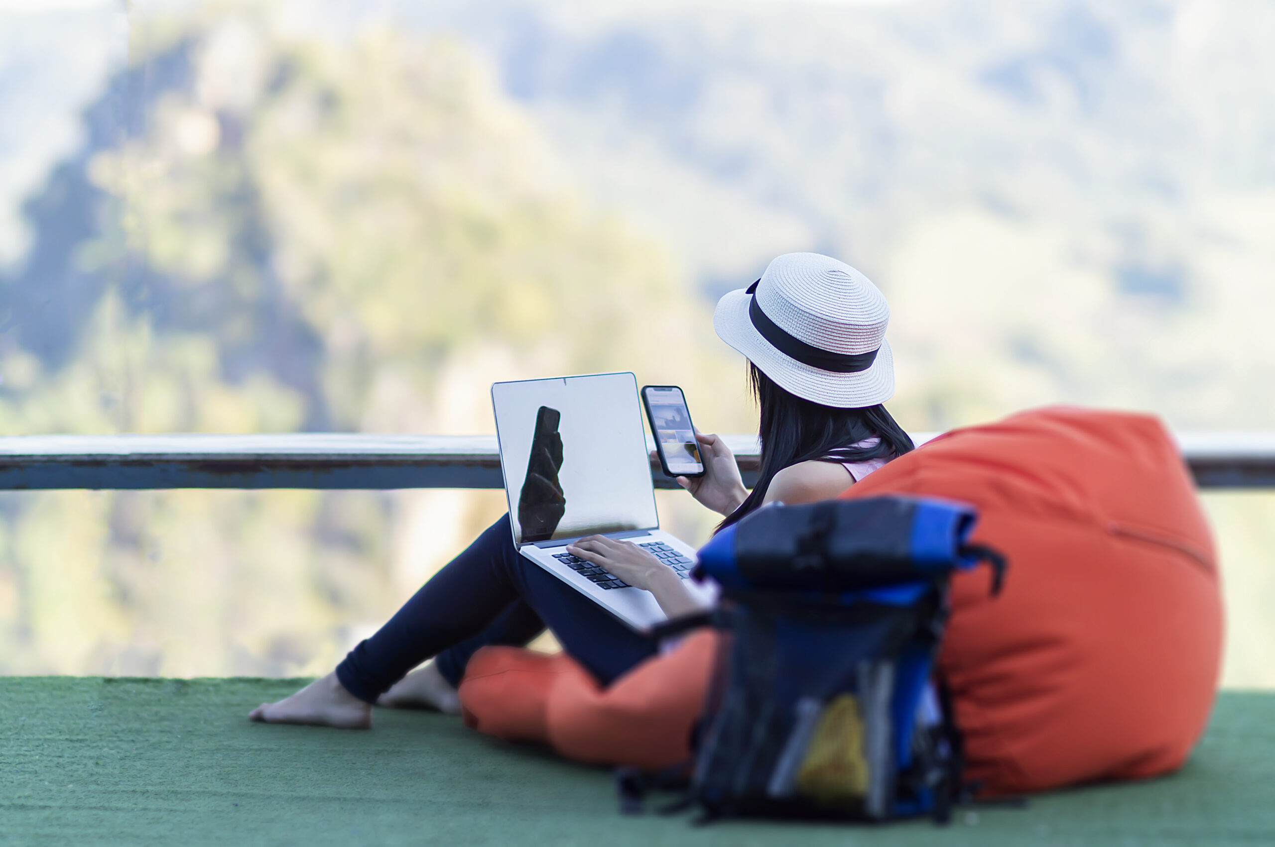 Influencer working remotely with laptop and phone, backpack nearby. Mountain view backdrop.