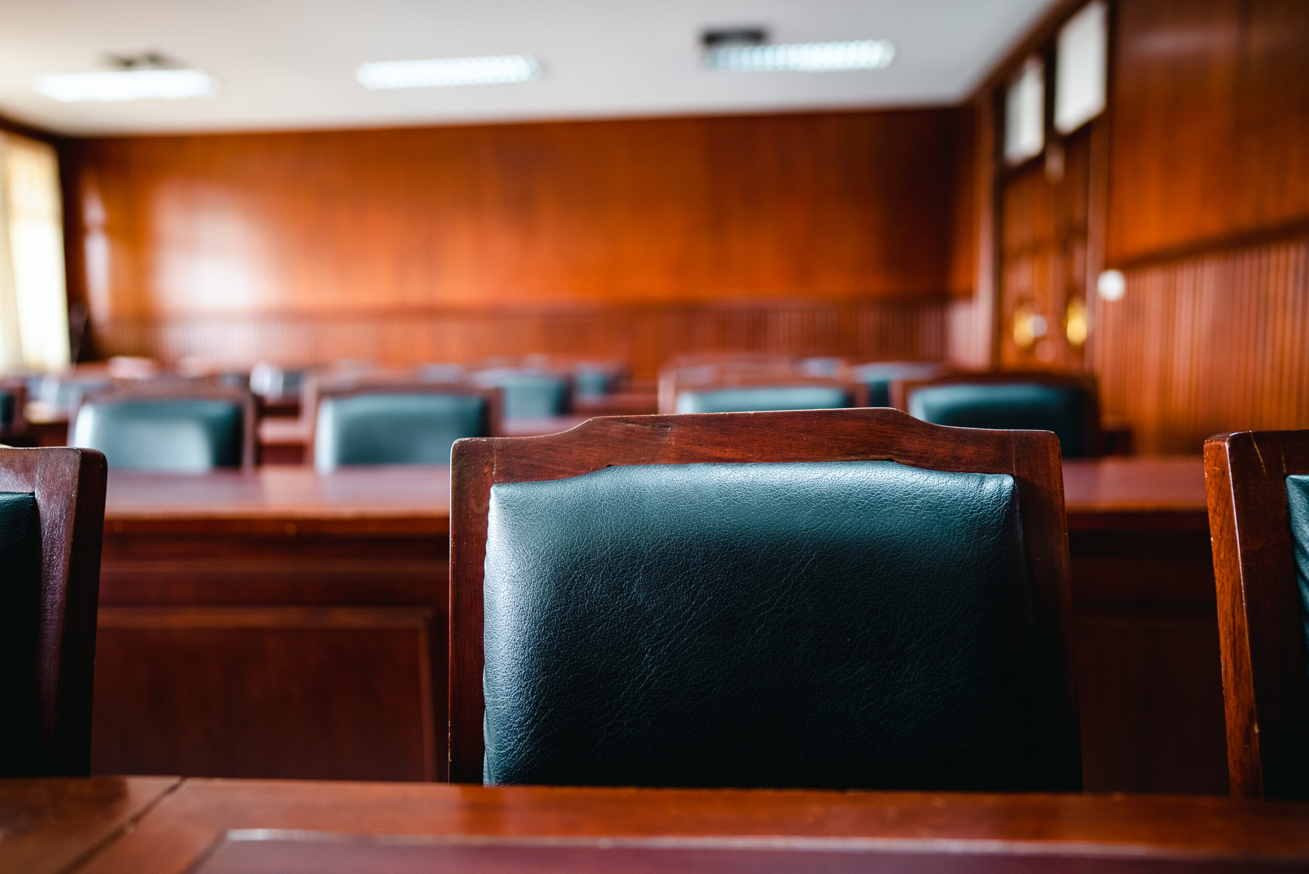 Empty courtroom with wooden benches and leather chairs.