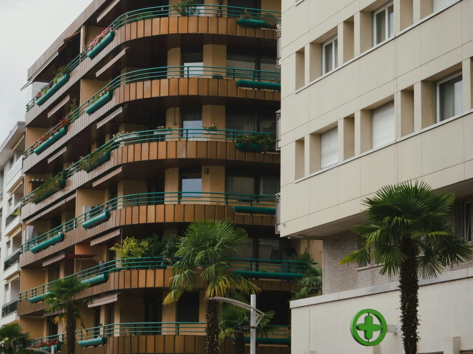 Apartment building with curved balconies and green railings next to a building with a green cross logo.