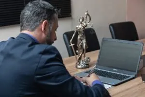 Lawyer reviewing documents on laptop with Lady Justice statue on desk.