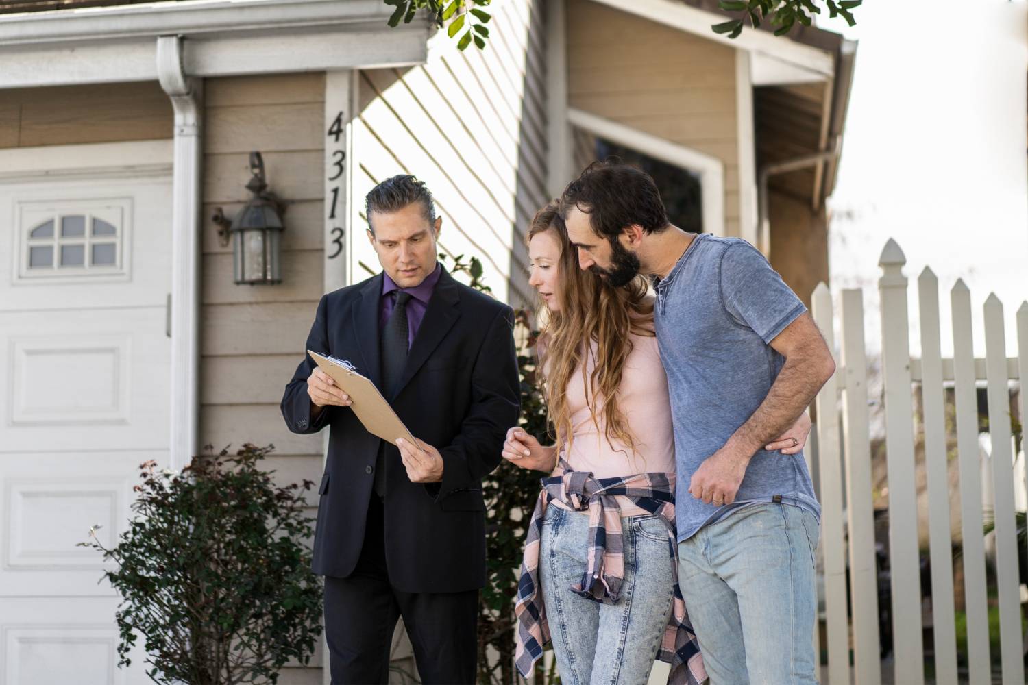 Real estate agent showing a young couple a house, reviewing documents on a clipboard.