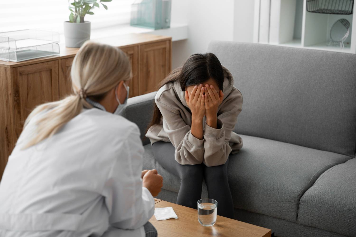 Woman in therapy session, covering her face, next to a glass of water.