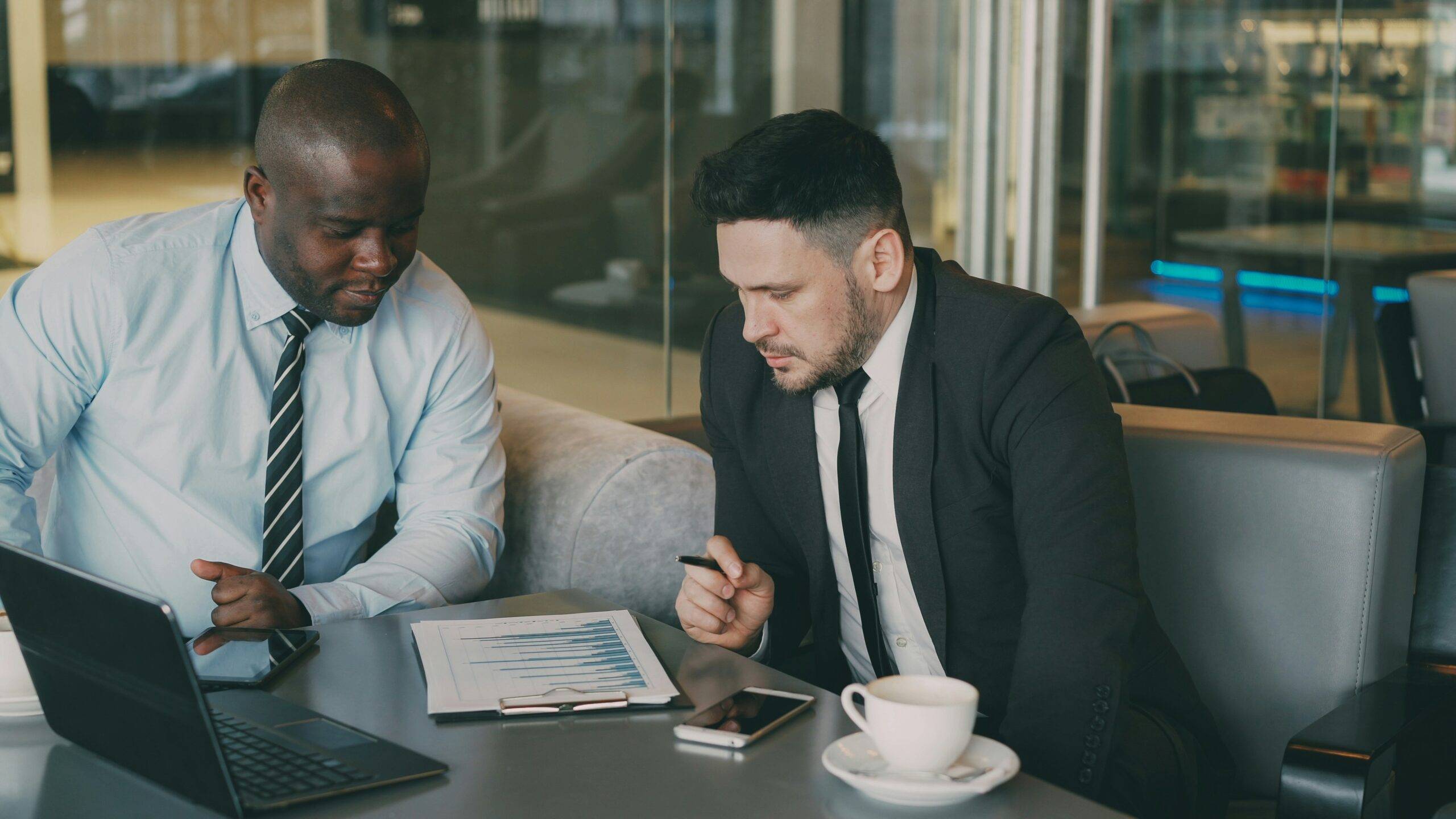 Two businessmen reviewing tax data charts at a cafe, discussing financial strategy.